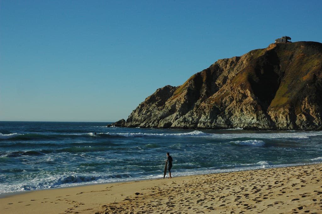 Surfers in those last few waves before sunset, clear winter day, blue sky, hill, Gray Whale Cove beach, old World War II bunker, Pacific Coast, near San Francisco, California, USA