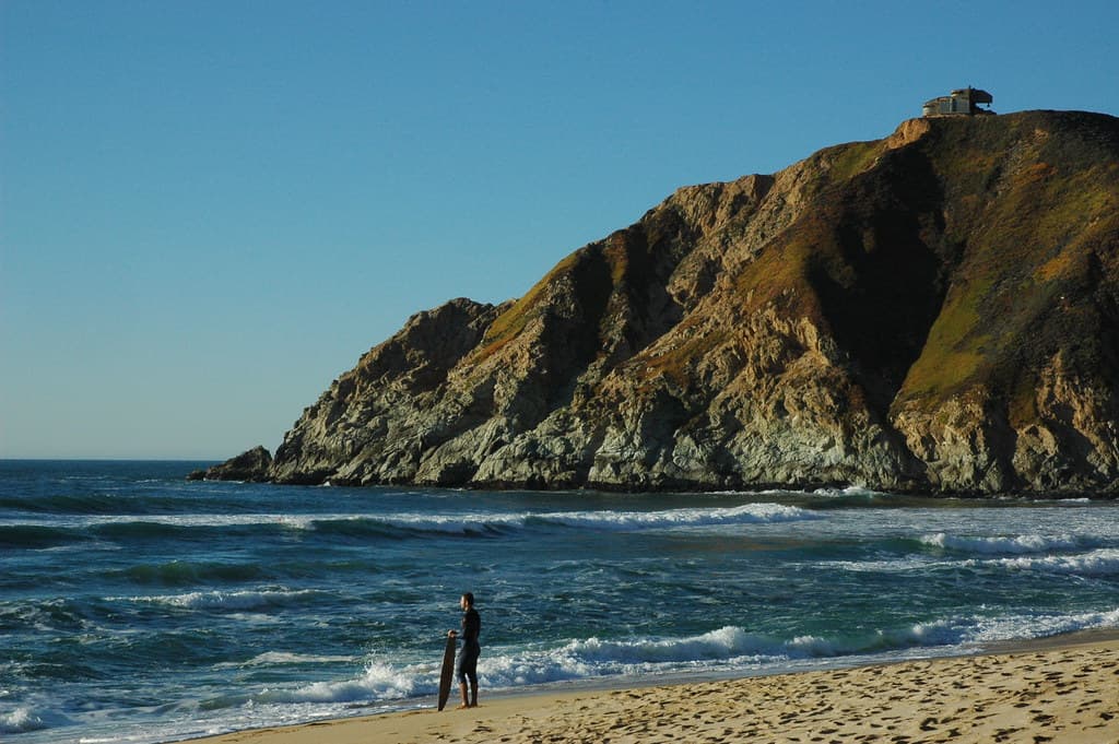 Surfer Standing on the beach watching Gray Whale Cove, California, USA