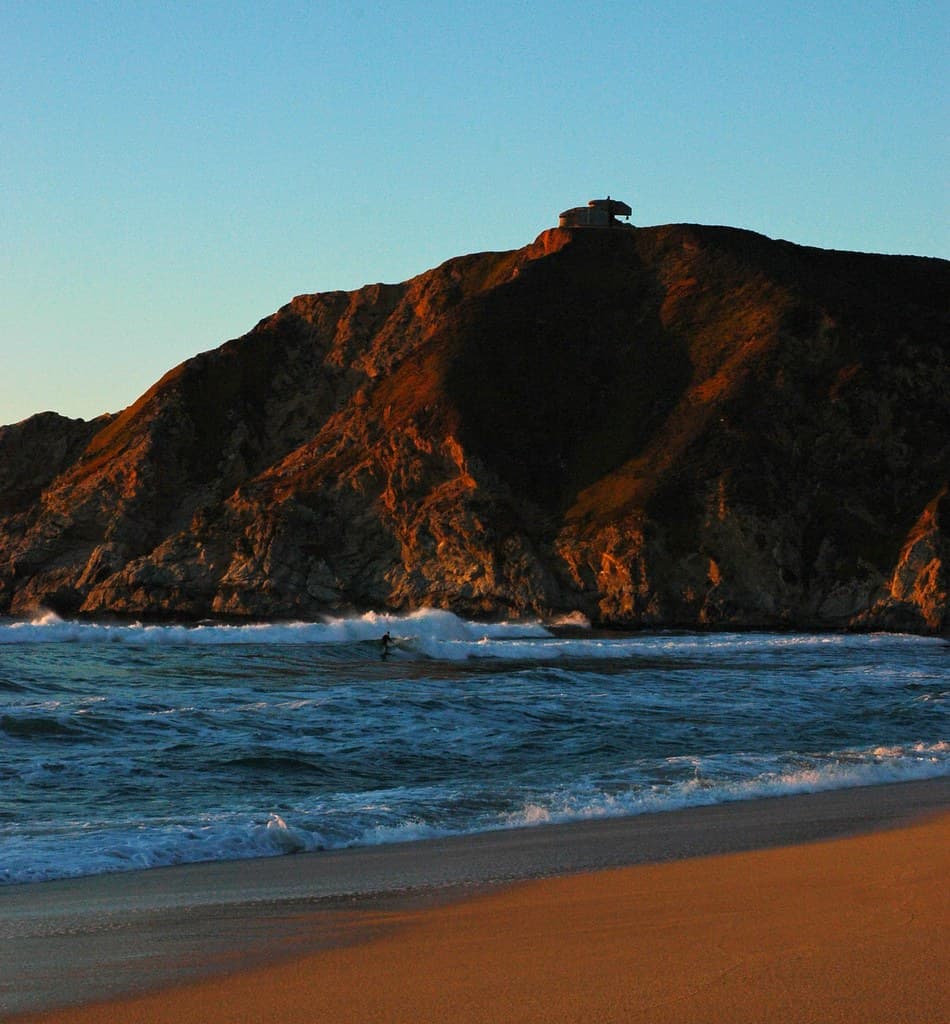 Surfing at sunset under the abandoned WWII Bunker, Gray Whale Cove, California Coast, USA
