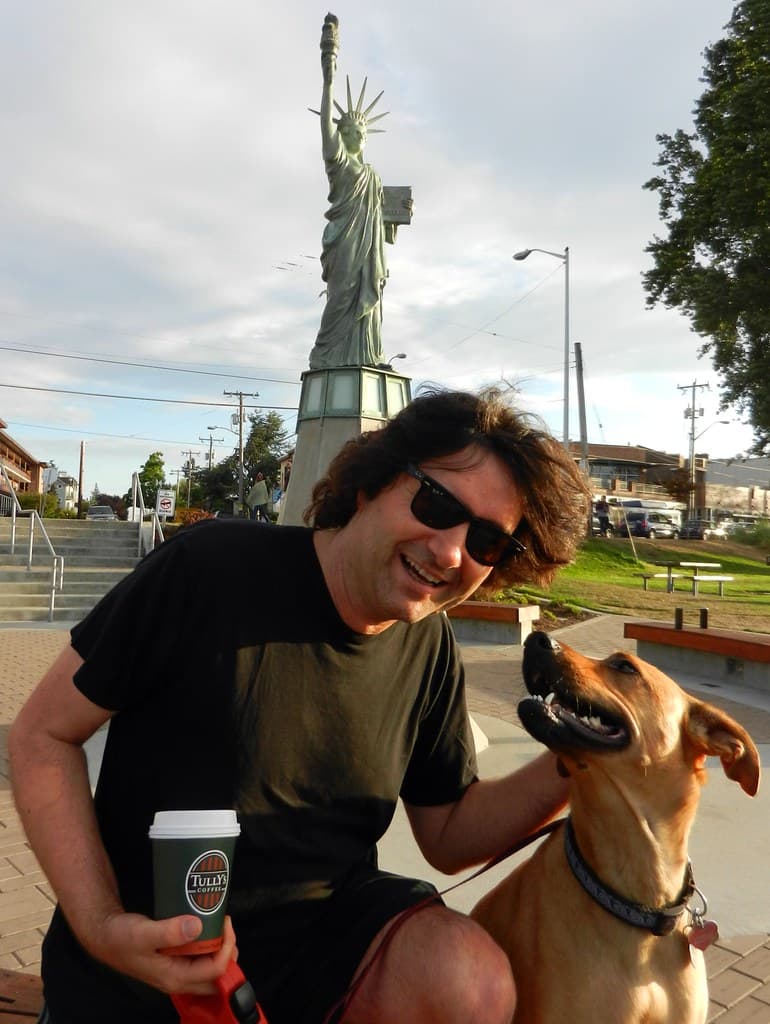 Behind sunglasses, Nick Boseck smiles with a cuppa Tully's joe, Rosie the dog, under the Statue of Liberty at Alki Beach, West Seattle, Washington, USA