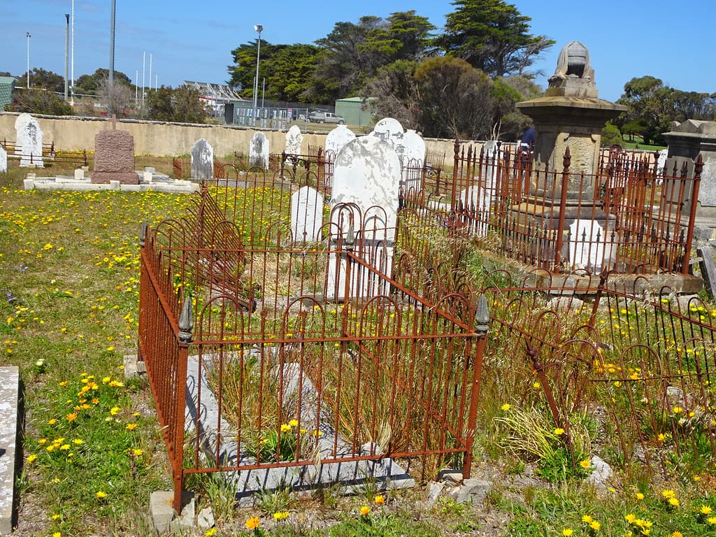 Robe historic port on Guichen bay. Rusty cast iron fence surrounds on graves in the cemetery. Gazanias flowering.