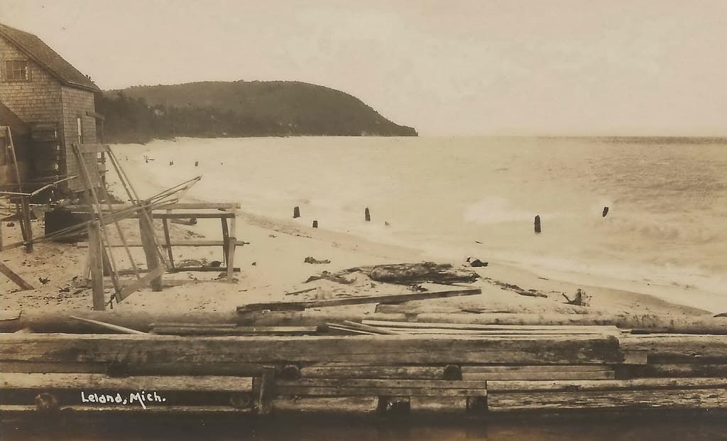 NW Leelanau Leland MI RPPC c.1910 BEFORE HARBOR Carp River Outlet & Old Commercial Fishing Shanty on Beach looking South to Pyramid Point from the Town Beach looking Southwest PHOTOGRAPHER UNK2